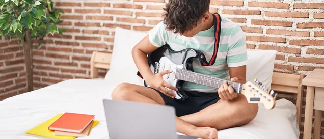 Young Male Playing Guitar In Bedroom